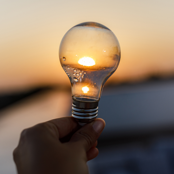 Elektriskā spuldze rokā uz saulrieta fona.