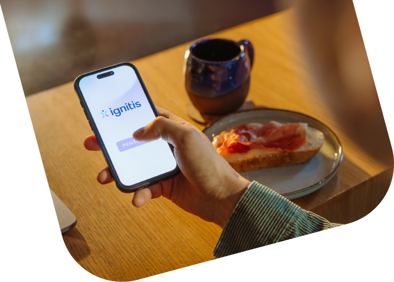 vīrieša roka ar mobilo tālruni, kurā attēlos Ignitis logo un poga pieteikties