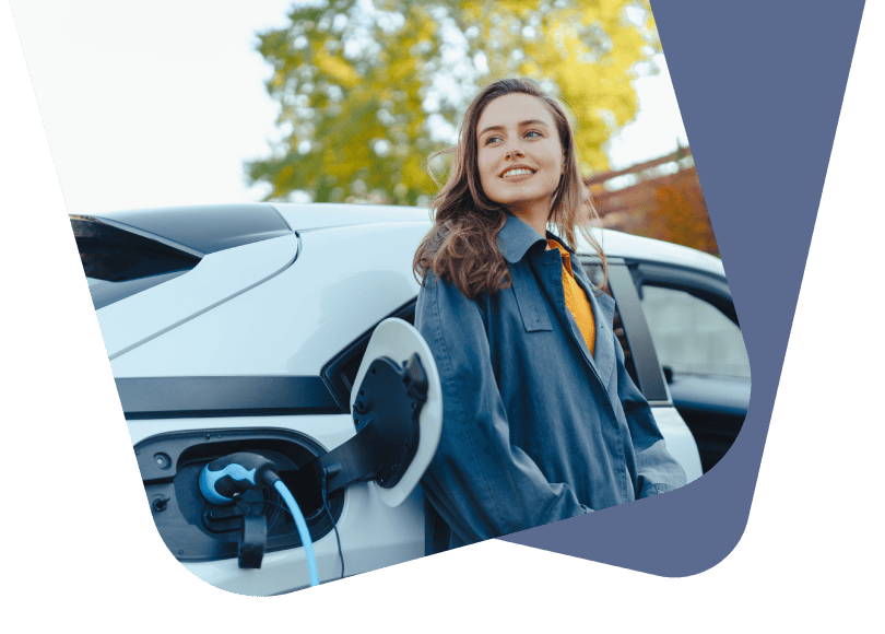 Sieviete smaidot atspiedusies pret balta elektroauto sāniem tā uzlādes brīdī; vizuāls materiāls par 'Naksnīgo' tarifu izdevīgai EV uzlādei mājās naktī.